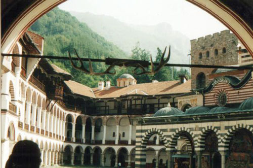 View of the Rila Monastery courtyard and the surrounding peaks from the Doupnitsa gate (1819). Parts can be seen of the northern (1817) and eastern (1816) wings of the monastery, Hrelyos tower (1335), and the church (1837). Photographer: A. Obretenov
